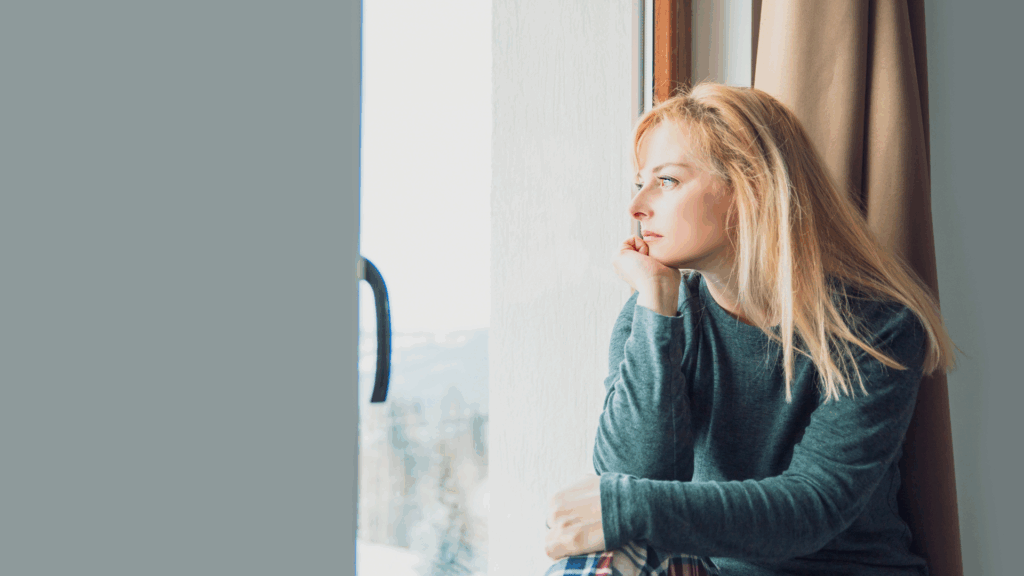 Blonde woman sitting by the window and dealing with brain fog.